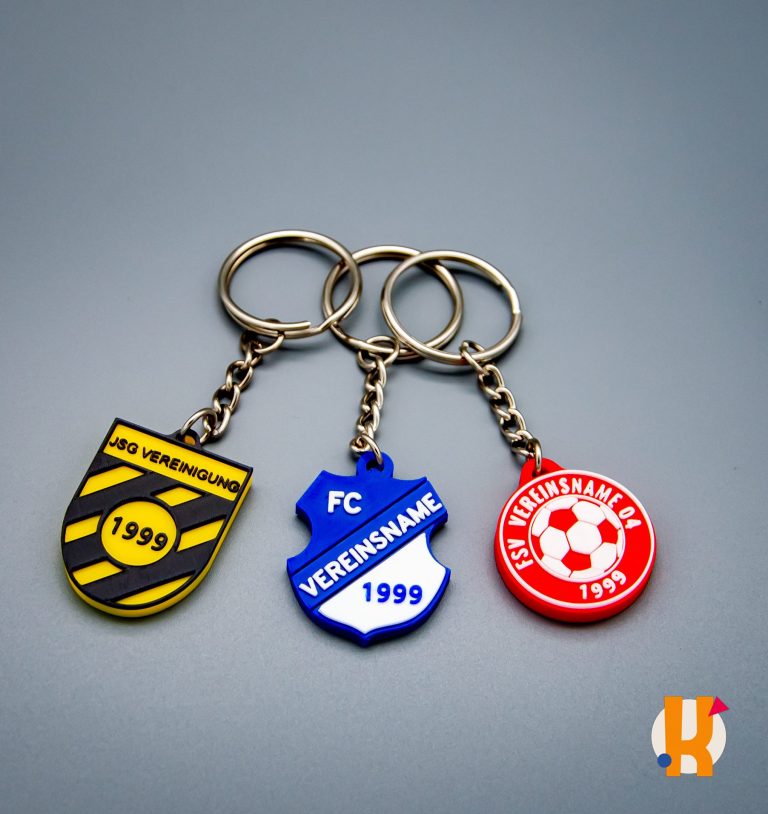 Drei Schlüsselanhänger in den Farben Schwarz-Gelb, Blau und Rot mit Fußballvereinslogos.